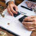 Persoană care calculează bugetul pe o masă de lemn.